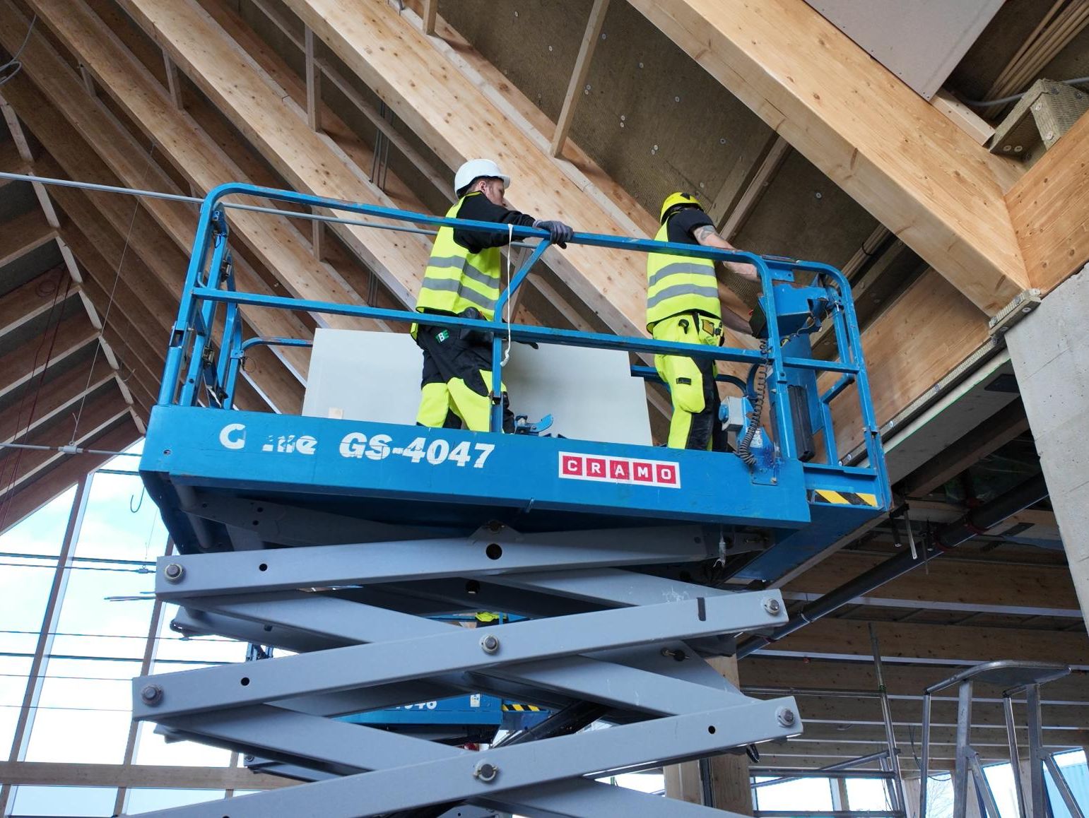 To arbeidere i lift under tak under bygging