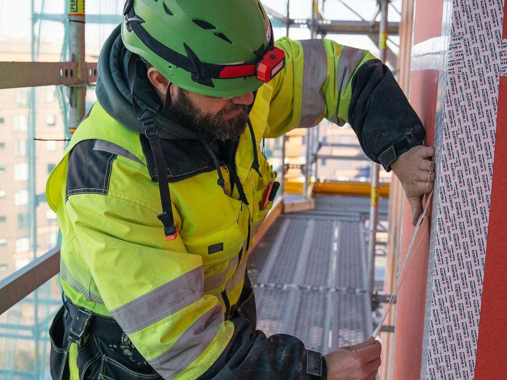 Bygningsarbeider monterer vindsperre på stillas ved fasadearbeid